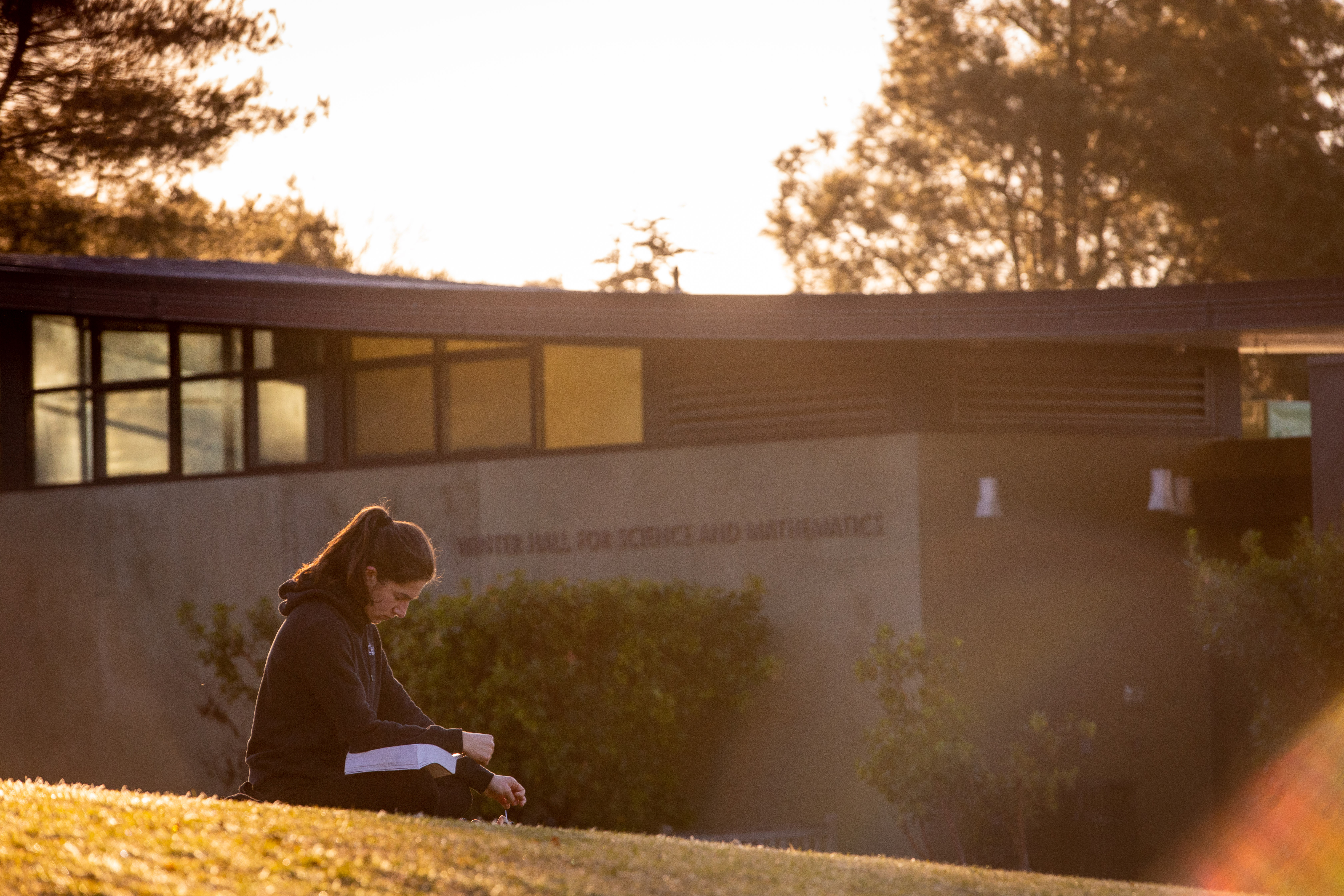 student sitting on grass in front of math building